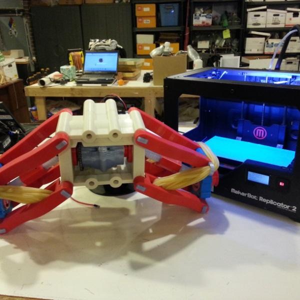 Часть механизма 3D-печатного радиоуправляемого автомобиля на полу рядом с 3D –принтером MakerBot Replicator 2